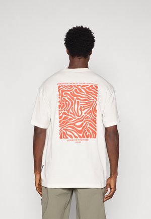 T-shirt en coton blanc avec un motif abstrait de vagues orange au dos, comportant le texte "FREERIDE WORLD TOUR" et "HOME OF FREERIDE" en bas.