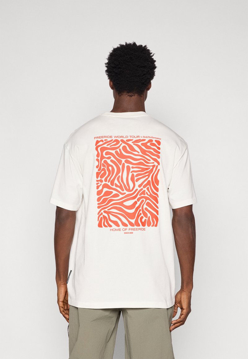 Λευκό βαμβακερό t-shirt με αφηρημένο πορτοκαλί σχέδιο κύματος στην πλάτη, με το κείμενο "FREERIDE WORLD TOUR" και "HOME OF FREERIDE" στο κάτω μέρος.