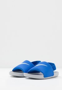 Blue slide sandals with a smooth upper, open-toe design, and a grey textured sole. Features a white logo on the front strap.
