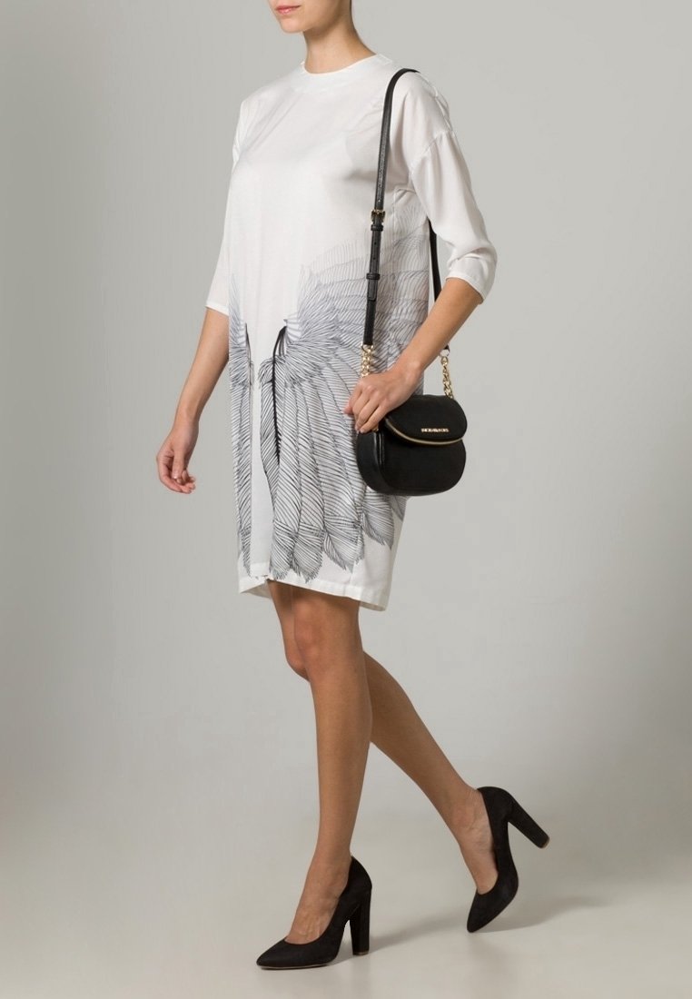 Abito bianco a maniche corte con un design stampato che ricorda piume nere; abbinato a una piccola borsa nera e scarpe con tacco alto nere.