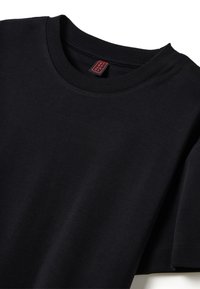 T-shirt di cotone nero con scollo tondo, maniche corte e una texture liscia. Presenta un'etichetta rossa sulla parte interna dello scollo.