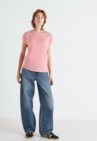 Rød og hvit stripete t-skjorte med korte ermer, kombinert med blå vid utlegging jeans. Sorte sneakers med hvite såler fullfører antrekket.