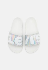 Sandales blanches à glissière avec une bride irisée portant de grandes lettres blanches, matériau lisse et semelle intérieure texturée.