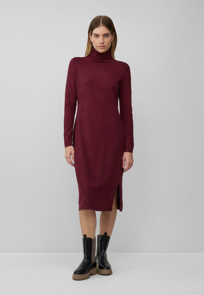 Bordeaux-farbenes Langarmkleid mit hohem Hals und seitlichem Schlitz, gefertigt aus einem weichen Material, kombiniert mit schwarzen derb-sohlen Knöchelstiefeln.