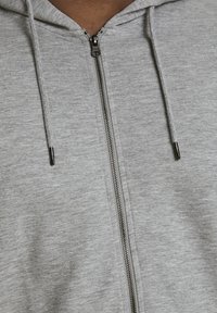 Haut à capuche zippé gris en tissu doux, avec une fermeture éclair pleine longueur, des cordons de serrage et des finitions côtelées à l'ourlet et aux poignets.