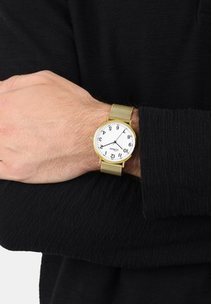 Goldmesh-Armbanduhr mit weißem Ziffernblatt, arabischen Ziffern und Stundenmarkierungen. Hand auf einem strukturierten schwarzen Ärmel positioniert.