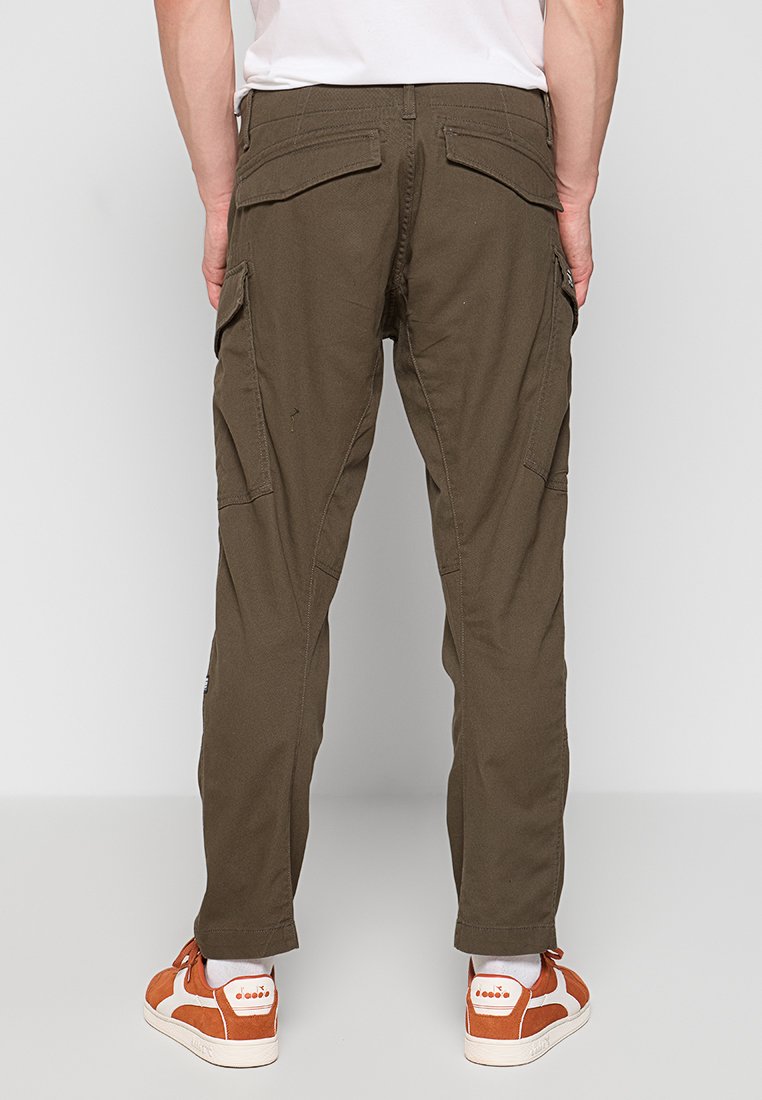 Pantalones cargo de tela verde oliva, con múltiples bolsillos laterales, corte recto y puños elásticos. Llevados con zapatillas naranjas y blancas.