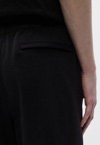 Τα μαύρα παντελόνια φούτερ διαθέτουν ένα κομψό, ματ φινίρισμα με μινιμαλιστικό σχεδιασμό. Μια διακριτική πίσω τσέπη είναι ορατή, ενισχύοντας τη λειτουργικότητα.