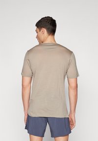 Korte mouwen, beige t-shirt van zacht materiaal, met een ronde halslijn en een ontspannen pasvorm, getoond op een model van achteren.