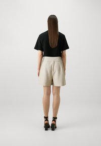 Svart topp med korte ermer kombinert med beige høyt liv shorts. Modellen har på seg chunky svarte helsandaler, med jevn tekstur og nøytrale farger.