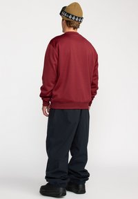 Un sweat-shirt bordeaux avec un col ras du cou, des poignets et un ourlet côtelés, associé à un pantalon navy à coupe ample et des chaussures noires, vu de dos.
