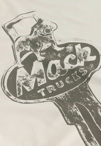 Bouledogue debout sur un logo vintage en forme de clé avec le texte en gras "Mack Trucks" sur un fond en tissu clair.