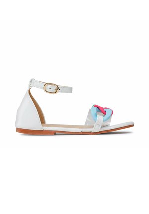 Biała płaska sandałka z paskiem wokół kostki, przezroczystym paskiem z przodu oraz niebiesko-różowym łańcuszkiem zdobiącym obszar palców.
