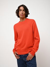 En orange ulltröja med rund halsringning och ribbade muddar, matchad med blå denimjeans. Tyget verkar mjukt med en slät textur.