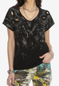 Camiseta negra de cuello en V con un patrón desgastado, adornos plateados y diseño de salpicaduras de pintura. Mangas cortas con detalles recortados.