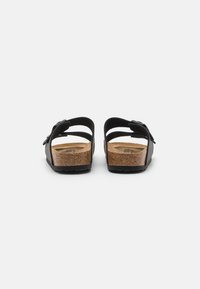 Black sandals with two adjustable straps, cork footbed, and rubber outsole. Rear view shows minimalist design and sturdy construction.