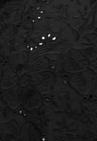 Μαύρο ύφασμα με λουλουδένια κεντήματα και μικρές οπές κομμένες με λέιζερ που σχηματίζουν ένα λεπτό, υφασμάτινο μοτίβο.