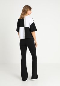 T-shirt cropped en bloc de couleurs noir et blanc avec des manches courtes, associé à un pantalon évasé noir et des chaussures blanches. Tissu à texture lisse.