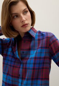 Overhemd met knopen, gekenmerkt door een multicolored geruit patroon in blauw, paars en rode tinten, met een omgeslagen kraag en lange mouwen.