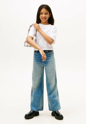 White cropped t-shirt with logo, light blue wide-leg jeans, and black chunky boots. Carrying a plaid shoulder bag.