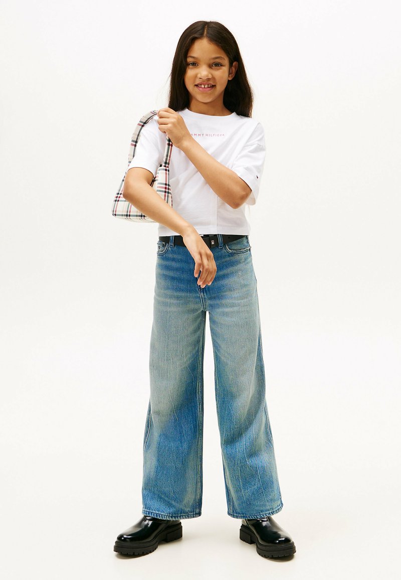 Hvid cropped t-shirt med logo, lyseblå vidde jeans og sorte chunky støvler. Bærer en skotsk skuldertaske.