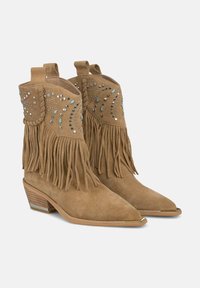 Botas de vaquero de ante marrón con punta afilada, detalle de flecos a los lados y tachuelas metálicas en un patrón de remolino en el eje. Tacón bajo y apilado.