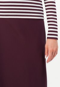 Majica s dolgimi rokavi z belimi in burgundskimi črtami, v kombinaciji z enobarvno burgundno krilo. Gladka tekstura tkanine in prilega silhueti.