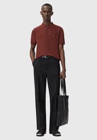 Polo shirt maroon con bottoni neri, abbinato a pantaloni neri. Gli accessori includono una borsa tote nera testurizzata e scarpe slip-on nere.