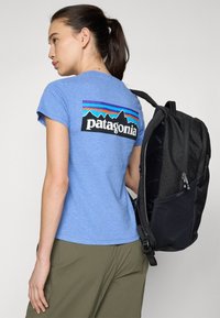 Mėlynas marškinėliai su retro juodu ir daugiaspalviu Patagonia logotipu ant nugaros, derinami su juodu struktūriniu kupriniu.