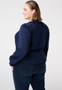 Donkerblauwe trui met lange pofmouwen, gestructureerde stof, ronde halslijn, getailleerd ontwerp, gecombineerd met donkerblauwe skinny jeans.