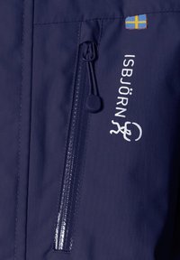 Mörkblå jacka med en dragkedjeficka och varumärket "ISBJÖRN" i vita bokstäver. Inkluderar en liten svensk flagga-patch.