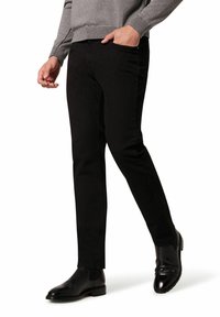 Czarne dżinsy z bawełny o dopasowanym kroju. Posiadają boczne kieszenie, subtelne szwy i są noszone z błyszczącymi czarnymi botkami typu chelsea.