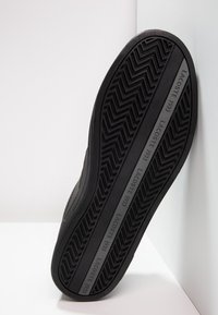 Svart sneakersula med fiskbensmönster, texturerad gummi och präglad "LACOSTE 1933" logodetail längs sidan.