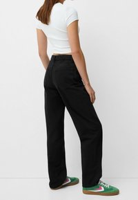 Jeans negros de tiro alto con diseño de pierna recta, bolsillos traseros y una tela texturizada. Combinados con zapatillas verdes y rosas.