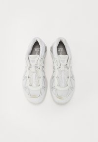 Bílé sportovní boty se síťovaným svrchním materiálem, reflexními prvky, elastickými tkaničkami a zaoblenou špičkou. Mají polstrovaný límec a odpruženou podrážku.