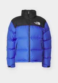 Veste matelassée isolante bleu et noir avec fermeture éclair à l'avant, deux poches latérales, col haut et logo The North Face sur la poitrine.
