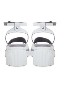 Sandales blanches à dos ouvert avec une semelle en plateforme texturée et un accent gris. Elles disposent d'une sangle à boucle et d'un dessus en cuir lisse.