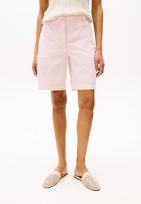 Ljusrosa bomullsshorts med rak skärning, som har en knappstängning och rullade fållar. Matchas med öppenvävsbeiga slip-on skor.