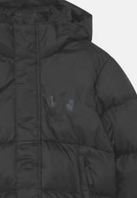 Černá vyteplená bunda s kapucí, má prošívané části, lesklý detail loga a boční kapsu na zip. Hladká textura.