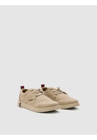 Zapatos casuales beige con parte superior de tela suave, punta redonda, cierre con cordones y un acento oscuro contrastante en el talón. Suela de goma texturizada.