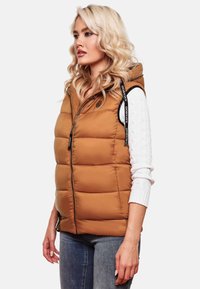 Gilet rembourré beige avec fermeture éclair à l'avant, design à coussins verticaux et capuche. Accentué par des bandes noires sur les épaules comportant un logo.
