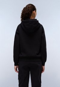 Zwarte hoodie met een voorste kangoeroezak en ribgebreide boorden. De stof lijkt zacht en getextureerd, met een ontspannen ontwerp en kap.