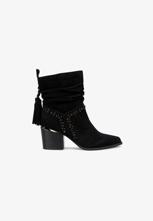 Stivale alla caviglia in suede nero con un design morbido, decorato con borchie e un tacco robusto. Presenta un dettaglio a nappina sul lato.
