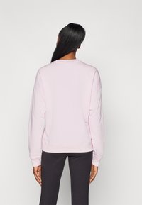 Sudadera de color rosa claro con hombros caídos y puños acanalados, combinada con leggings oscuros. La tela parece suave y ligeramente texturizada.