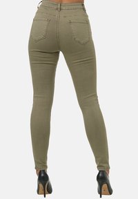 Pantalones skinny verdes oliva hechos de algodón elástico, con cinco bolsillos y una cintura de altura media, combinados con zapatos de tacón alto negros.