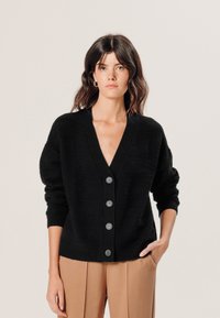 Schwarze Strickjacke mit tiefem V-Ausschnitt, langen Ärmeln und fünf Knopfverschlüssen. Sie hat strukturierte Muster sowie gerippte Bündchen und Saum.