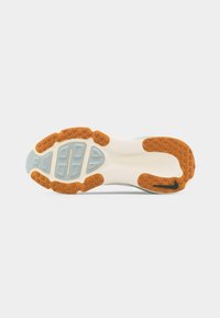 Σόλα παπουτσιού με λευκή βάση, πορτοκαλί ελαστικά τμήματα, γκρι ενθέματα πάτου και μικρό μαύρο λογότυπο Nike κοντά στη φτέρνα σε απλό φόντο.