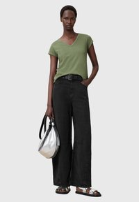 Grøn V-hals T-shirt, sorte brede bukser, sort bælte, sølv handbag og sandaler med sort-hvid strop. Ensfarvet baggrund.