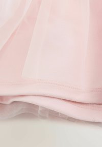 Gaiši rozā slāņaina auduma ar smalku sieta tilla pārklājumu un izšūtu apmali, attēlojot tekstūru un mīkstu kritumu.