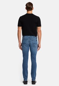 Hellblaue Jeans aus Denim mit Slim-Fit, ausgestattet mit zwei Gesäßtaschen und dezenten Nähten. Kombiniert mit einem schwarzen Kurzarmhemd.